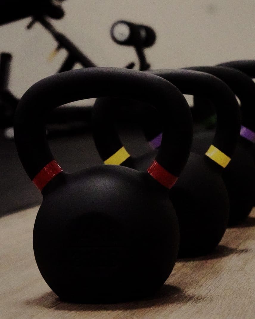 Row of color-coded kettlebells on the training floor at The Den